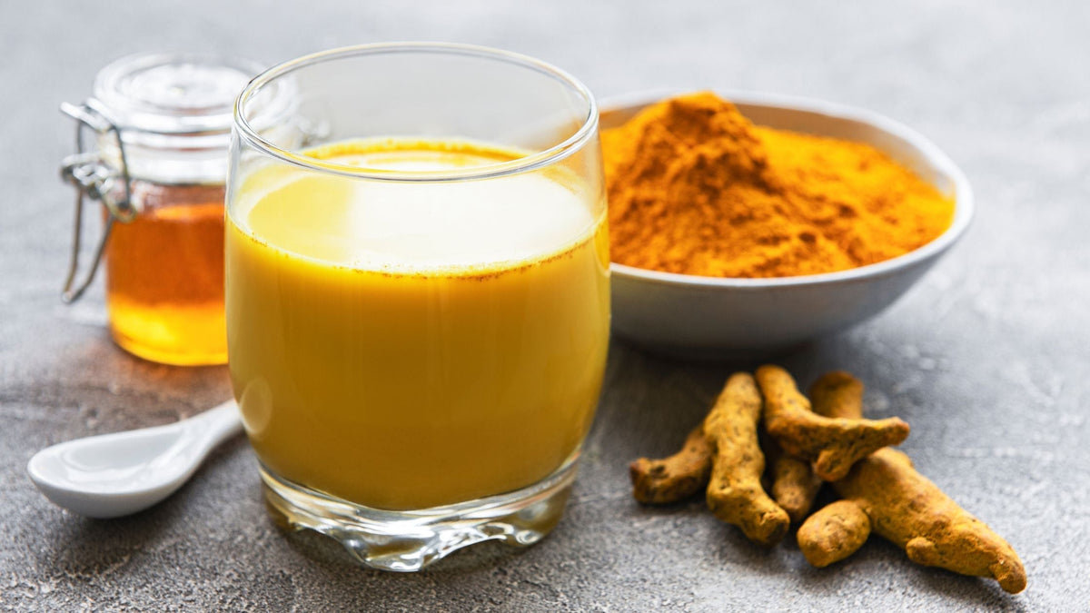 Golden turmeric milk in glass cup with powder and root