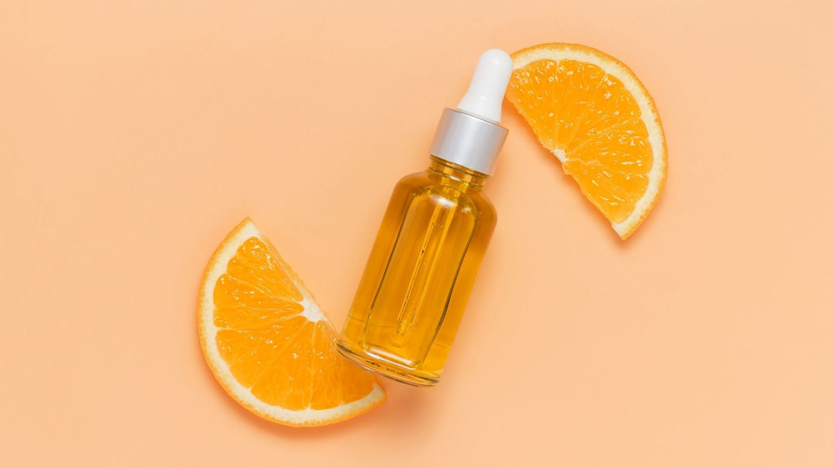 Facial oil bottle with vitamin C on sliced orange top view