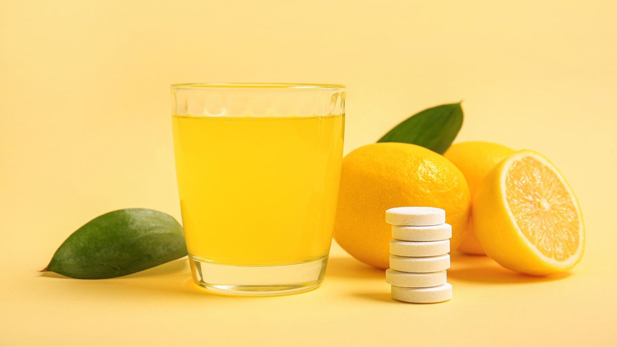 Glass of Vitamin C Tablet Dissolved in Water and Lemons on Beige Background