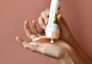 A person squeezing a tube of lotion on their hand