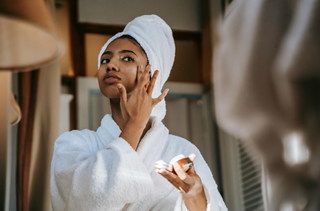 woman applying cream on face against mirror