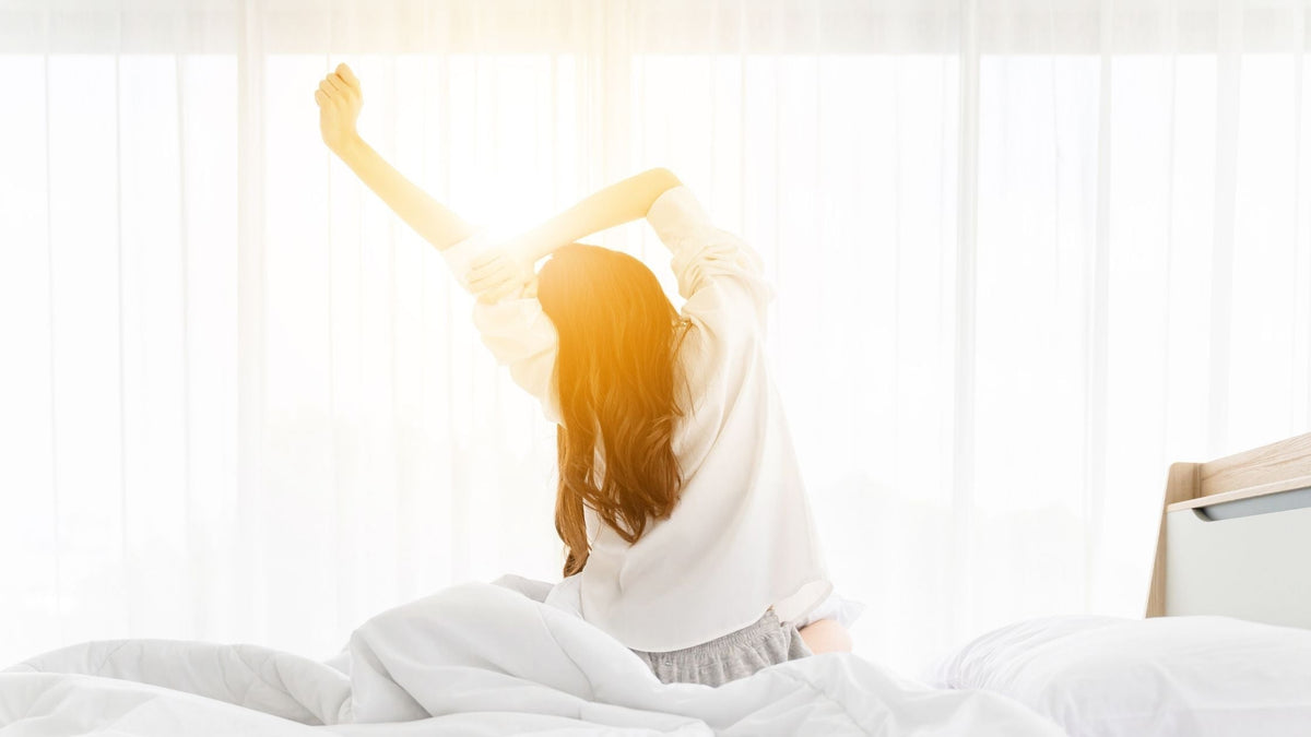 Woman waking up to sun shining through curtain
