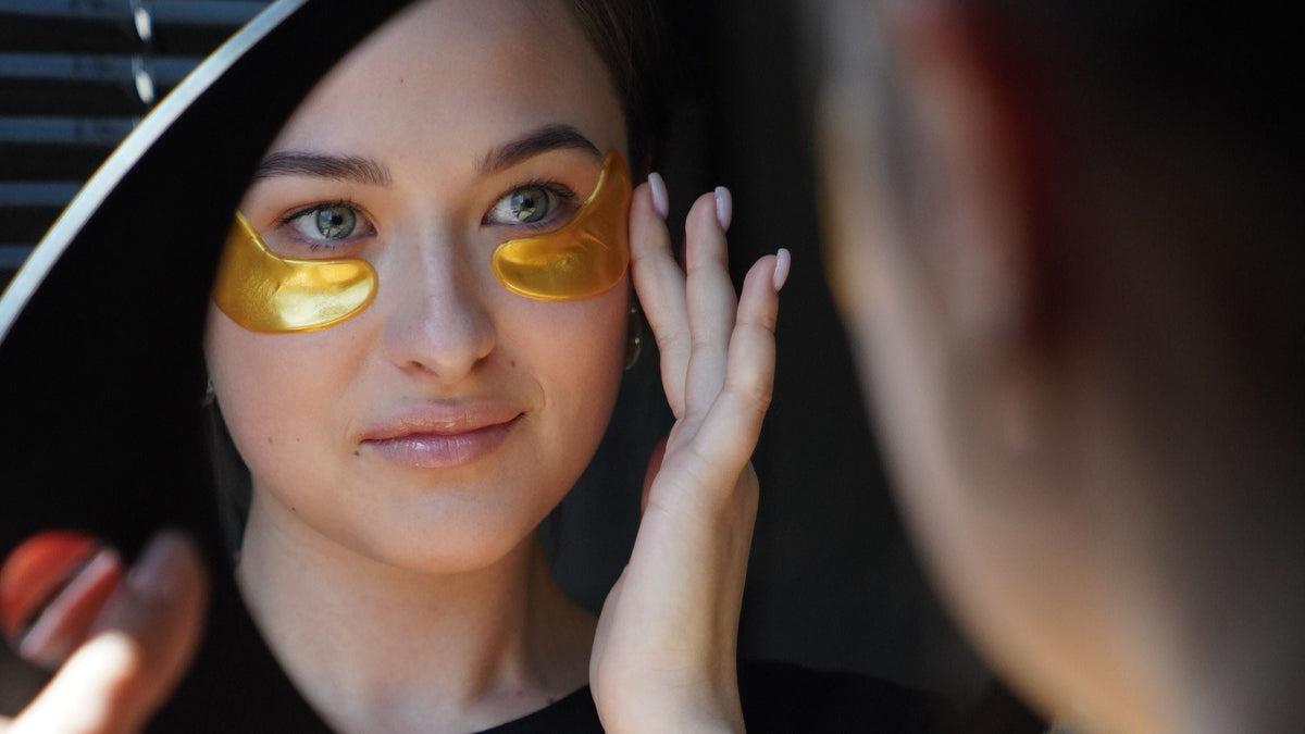 Women applying gold eye mask at night in front of mirror