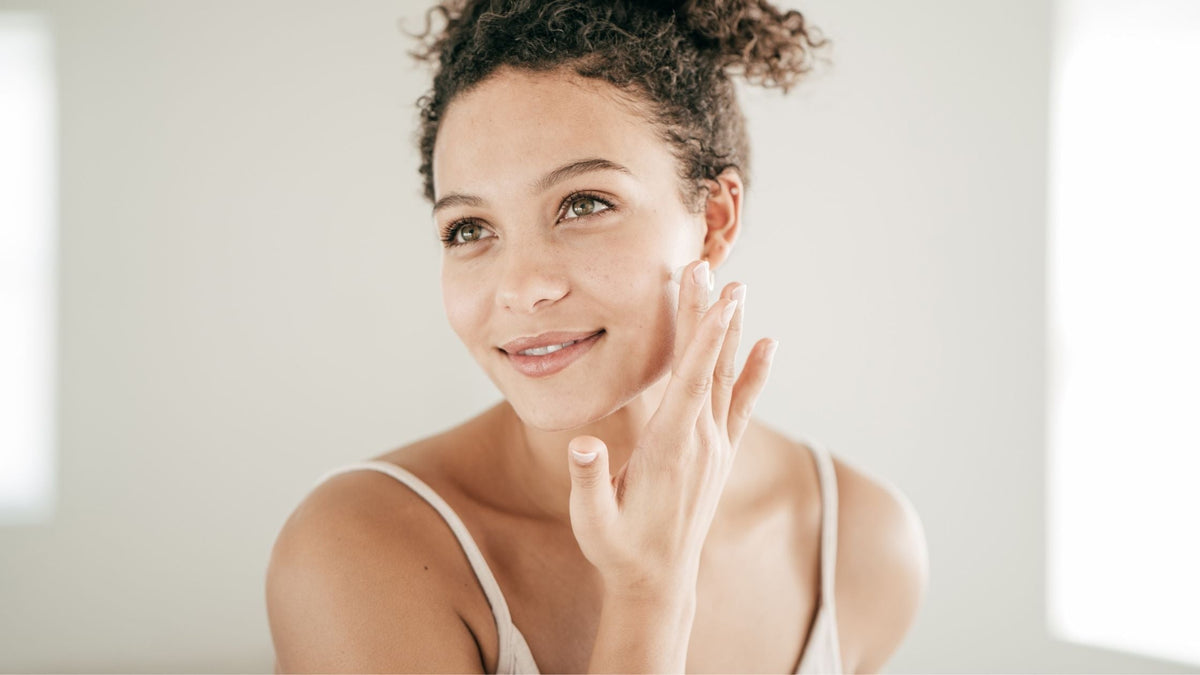 Young woman applying face cream in mirror