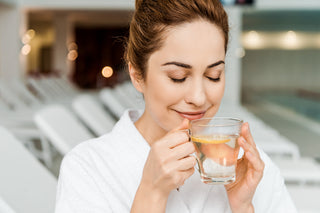 happy young woman with closed eyes holding cup with herbal drink and lemon while resting in spa