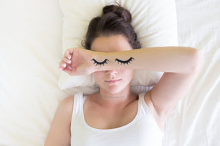 young woman in the bed with sleeping eyes painted on her arm and placed over her face